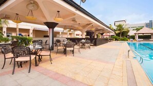 An outdoor pool area with lounge chairs and tables, a covered seating area, and a poolside bar.