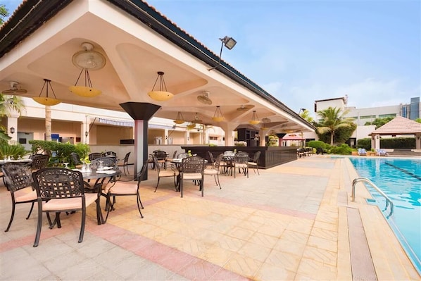 Ein Außenpoolbereich mit Liegestühlen und Tischen, einem überdachten Sitzbereich sowie einer Poolbar.
