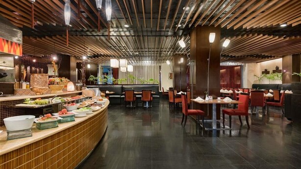 A restaurant with a curved buffet counter, seating area with tables and chairs, and a modern ceiling design.