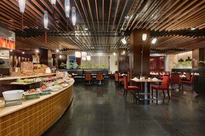 Un restaurante con una barra buffet curva, zona de estar con mesas y sillas, y un diseño de techo moderno.