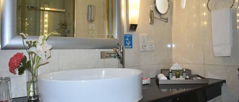 A modern bathroom with a large white sink, a mirror, a glass vase with flowers, and a black countertop.