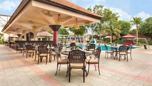 An outdoor pool area with multiple seating arrangements, including round tables and chairs, and a covered pavilion structure.