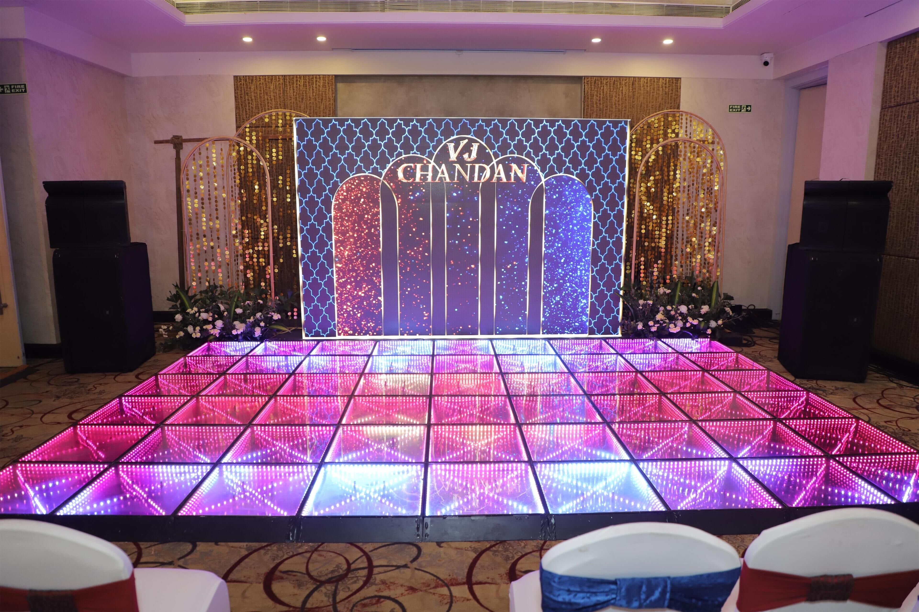 Un escenario con un telón de fondo de 'VJ Chandran', una pared estampada y un suelo con paneles iluminados.