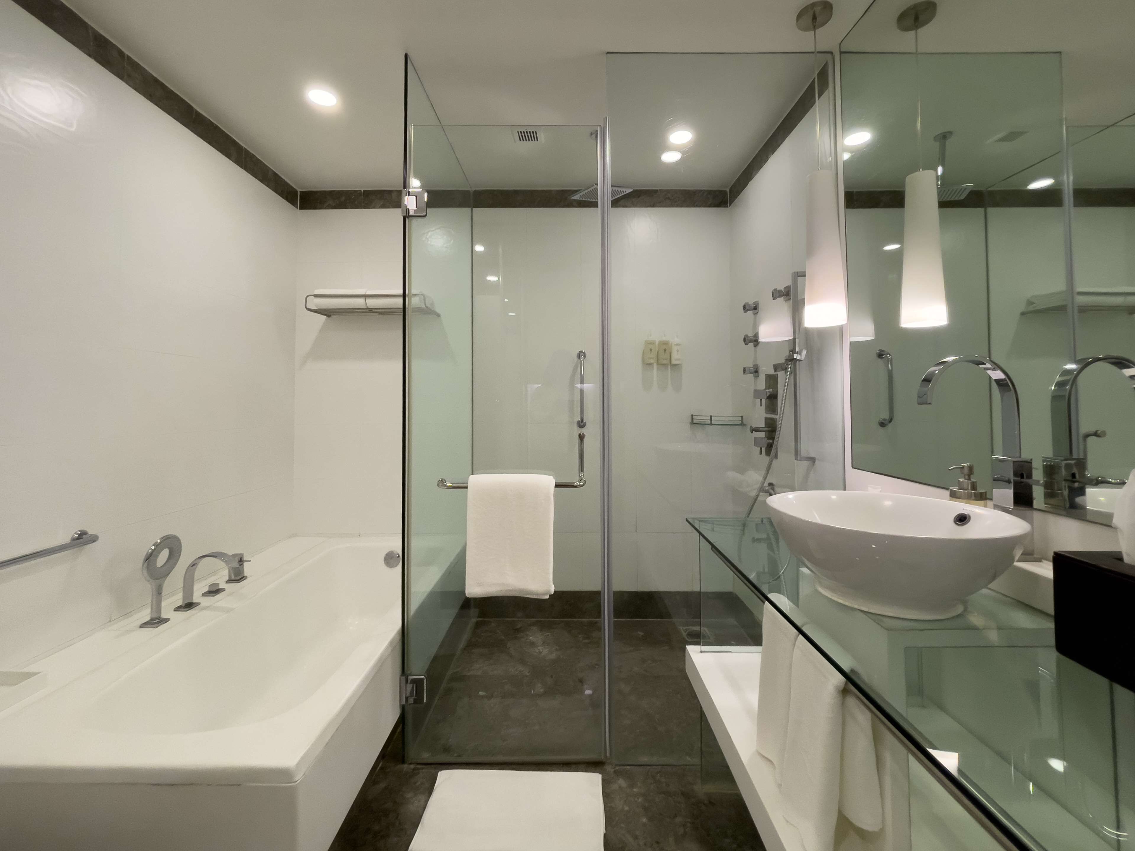 A modern bathroom with a glass-enclosed shower, a freestanding bathtub, and a large vanity with a glass countertop.
