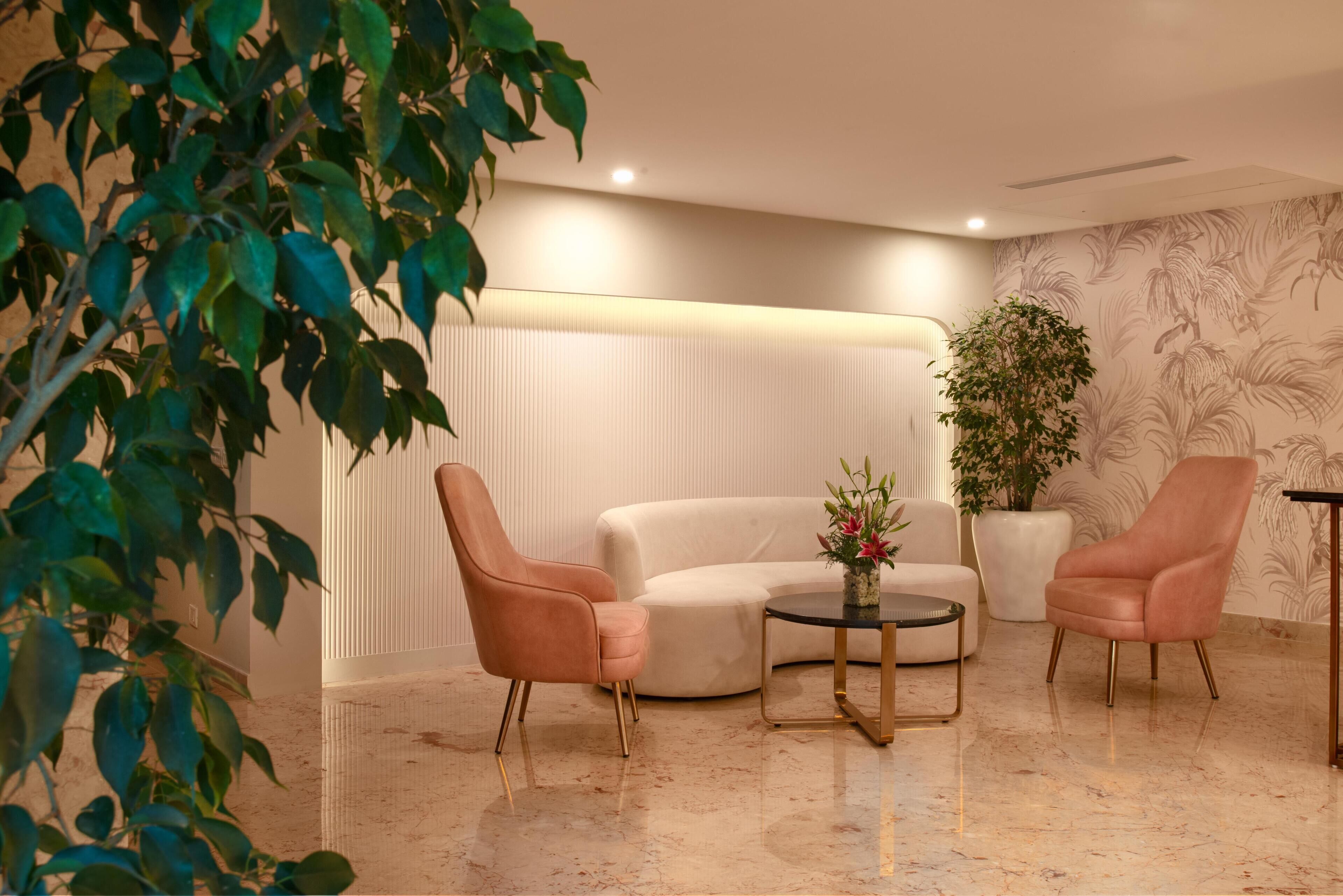 Un área de descanso moderna con sofá, dos sillones, una mesa de centro, una planta en maceta y una pared con diseño de hojas.