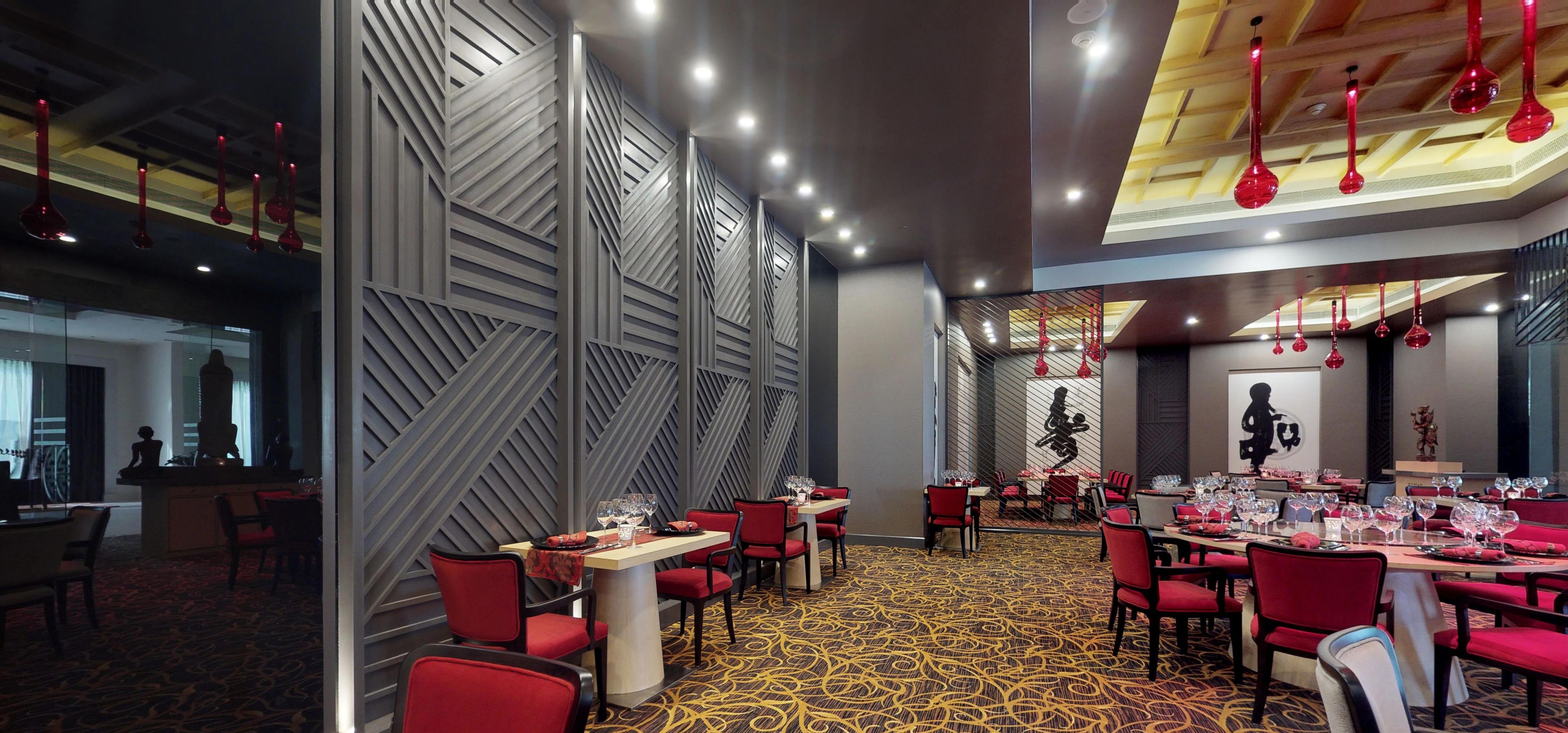 A modern restaurant with red chairs, a patterned carpet, and a geometric wall design.