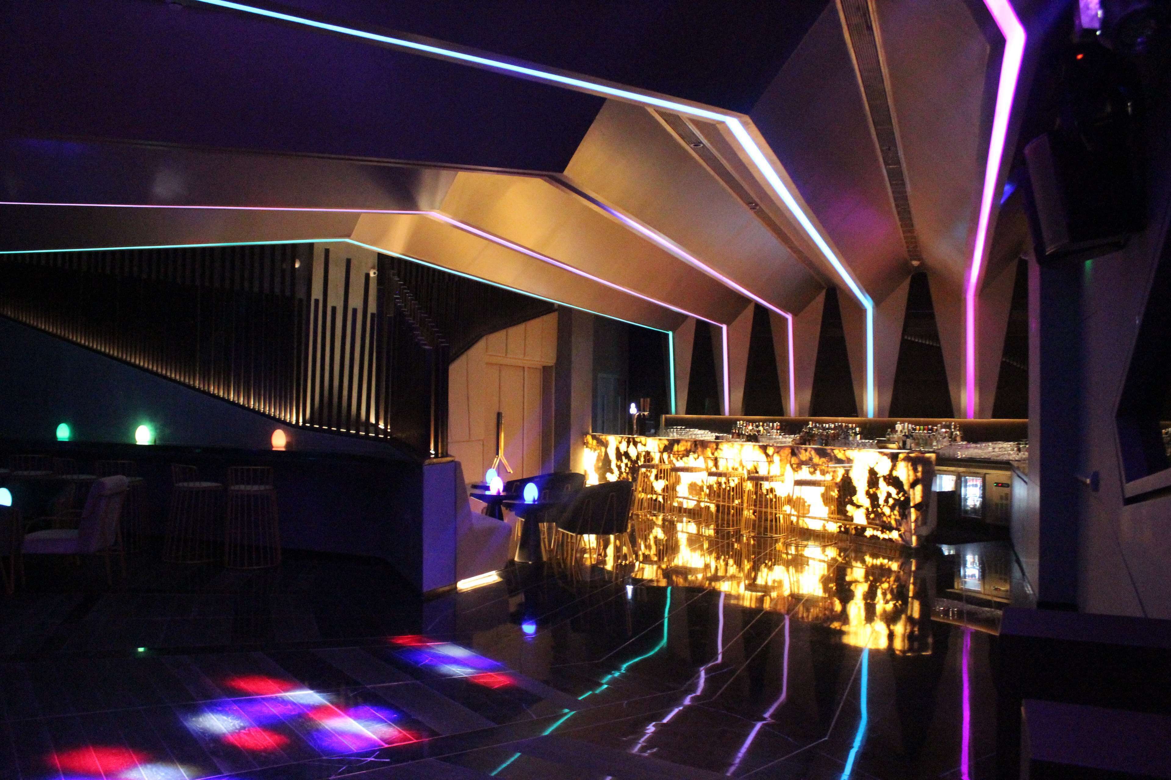 Uma área de bar moderna com piso refletivo, balcão elegante e iluminação ambiente.