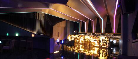 Uma área de bar moderna com piso refletivo, balcão elegante e iluminação ambiente.