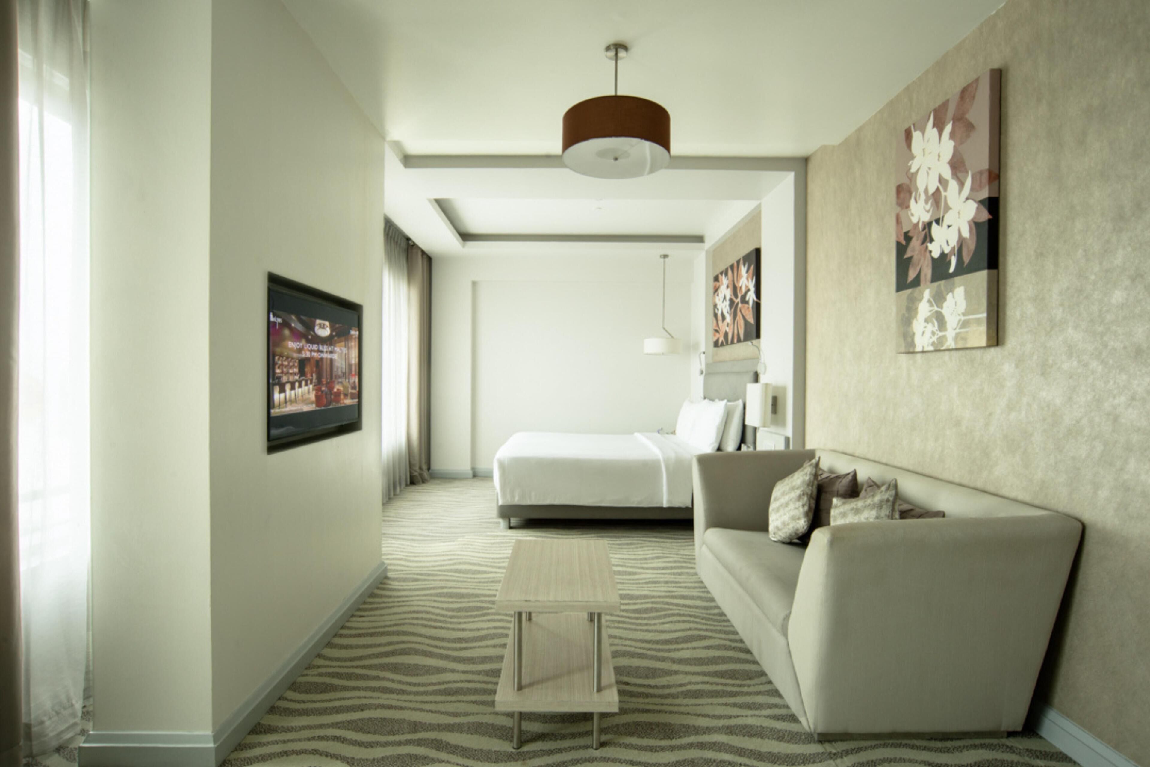Una habitación de hotel moderna con cama, sofá, una mesita y un amplio ventanal.