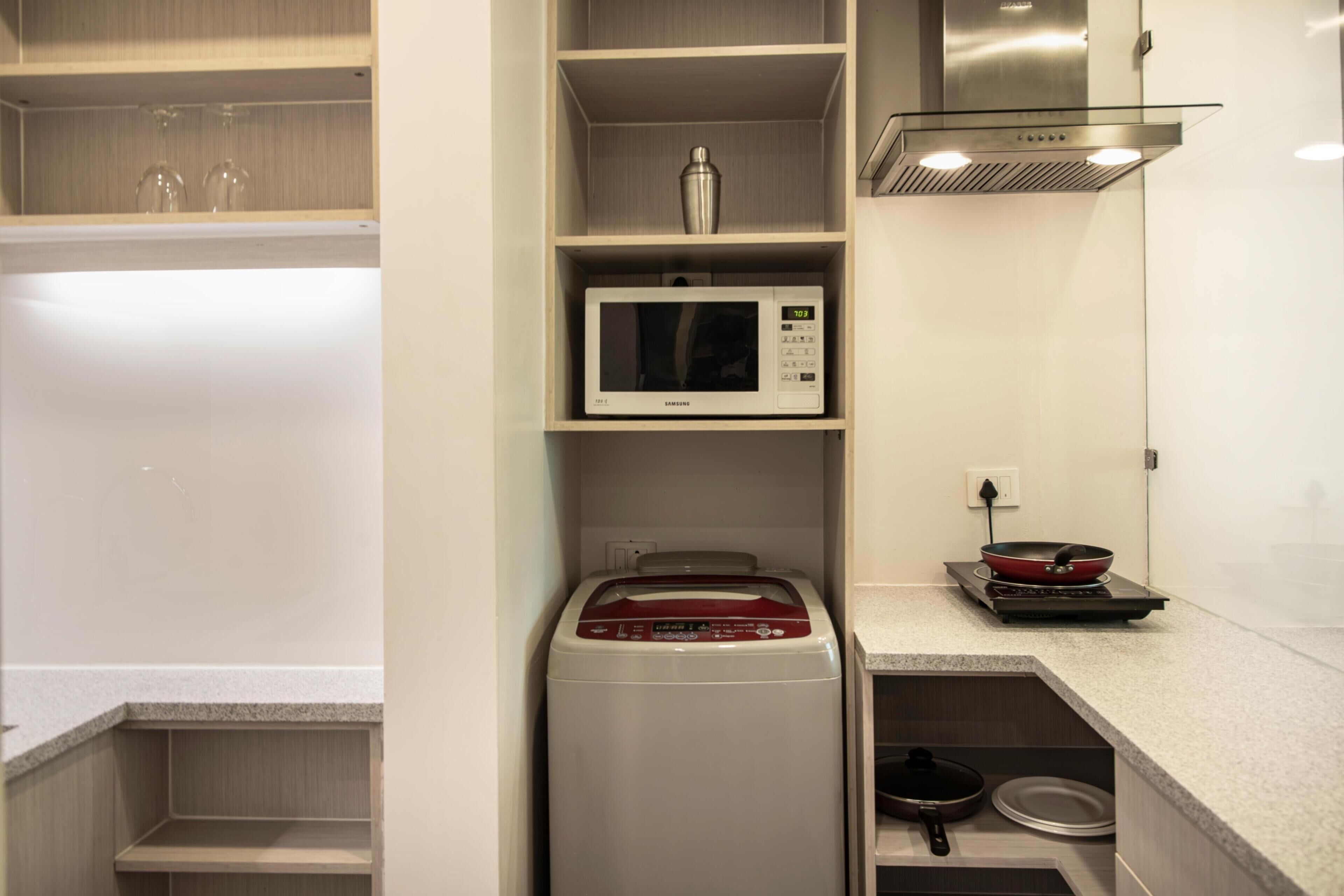 A compact kitchen with a microwave, a red appliance, and a frying pan on the counter.