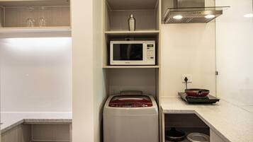 A compact kitchen with a microwave, a red appliance, and a frying pan on the counter.