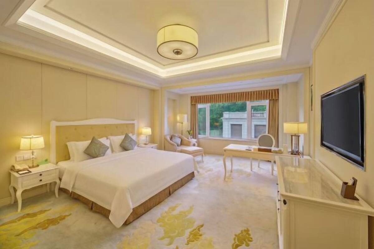 Een hotelkamer met een groot bed, nachtkastjes, een bureau, een stoel, een televisie en een raam met gordijnen.
