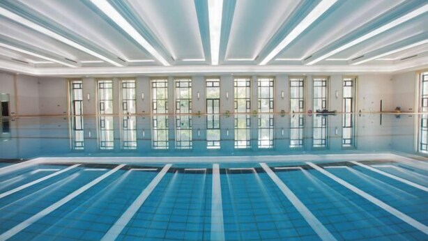 A large indoor swimming pool with clear blue water, surrounded by windows and a modern ceiling design. - Dongjiao State Guesthouse (Nanjing)