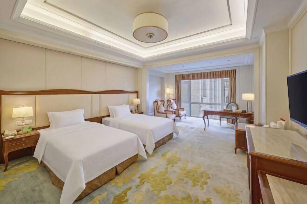 Hotelkamer met twee bedden, een bureau, een stoel, een televisie en een groot raam.