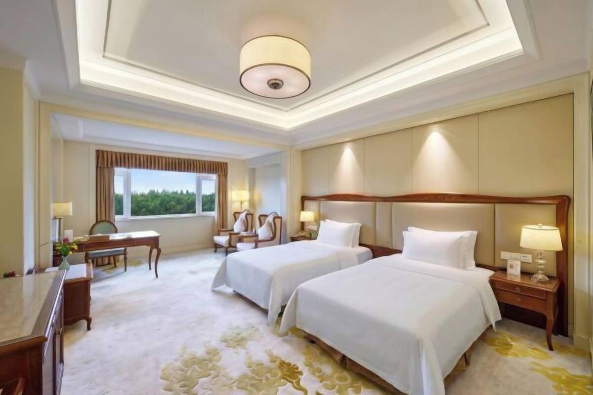 Een hotelkamer met twee bedden, een bureau, een stoel, een lamp en uitzicht op de omgeving.