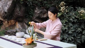 A person arranging a table with a purple cloth, white bowls, and a flower arrangement. - Dongjiao State Guesthouse (Nanjing)