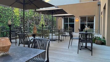 Een terras buiten met tafels en stoelen, omgeven door een muur met beplanting.