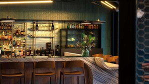 A bar area with multiple shelves of bottles, a marble countertop, and wooden bar stools. - Hotel Mercure Libourne Saint-Emilion (Libourne)