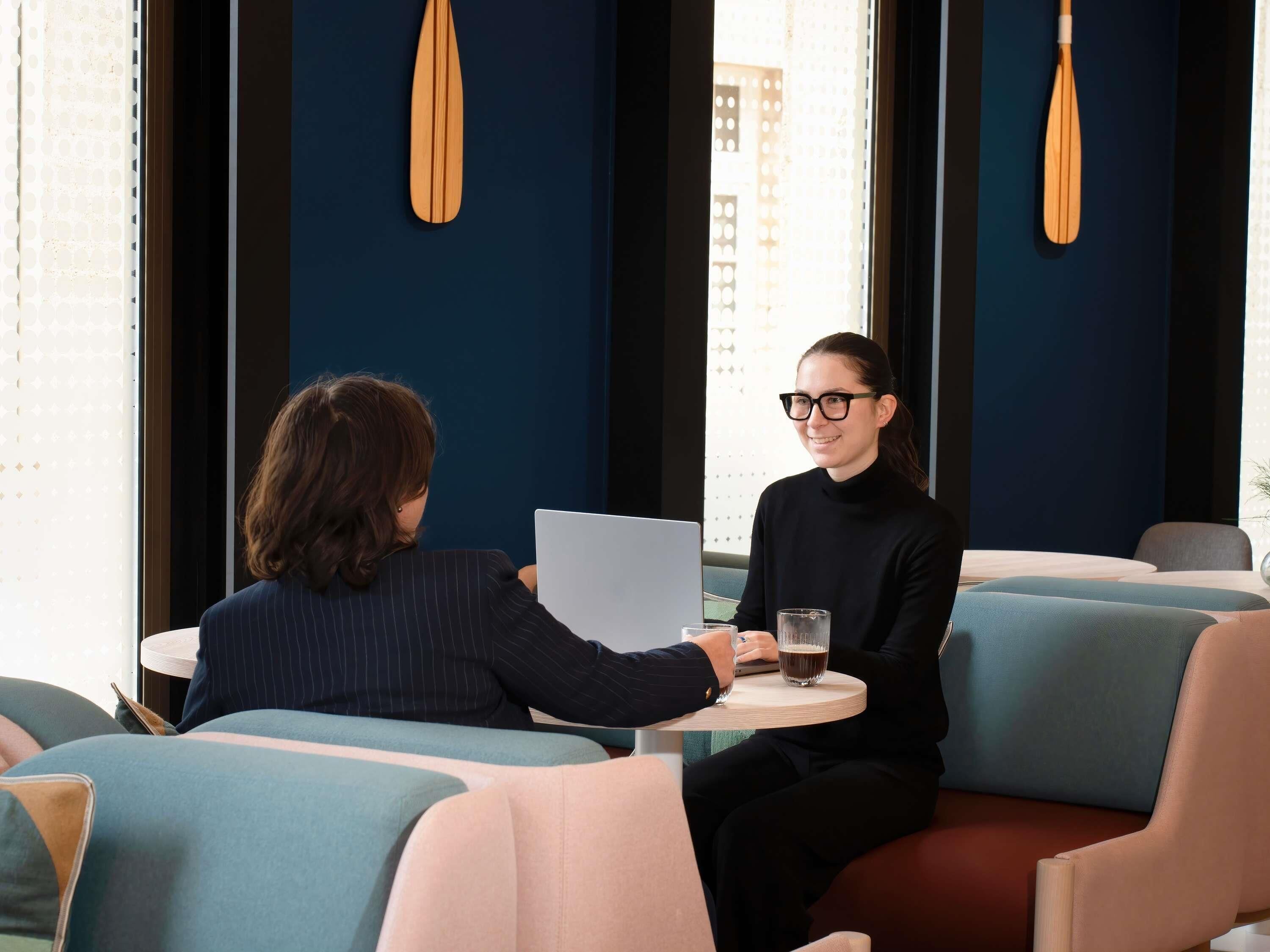 Dos personas sentadas en una mesa redonda en un interior moderno con paredes azules y detalles de madera.