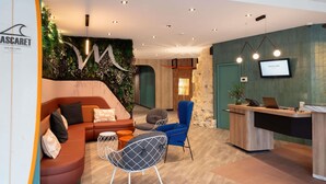 A modern hotel lobby with a reception desk, seating area with sofas and chairs, a wall with greenery, and a mounted TV screen. - Hotel Mercure Libourne Saint-Emilion (Libourne)
