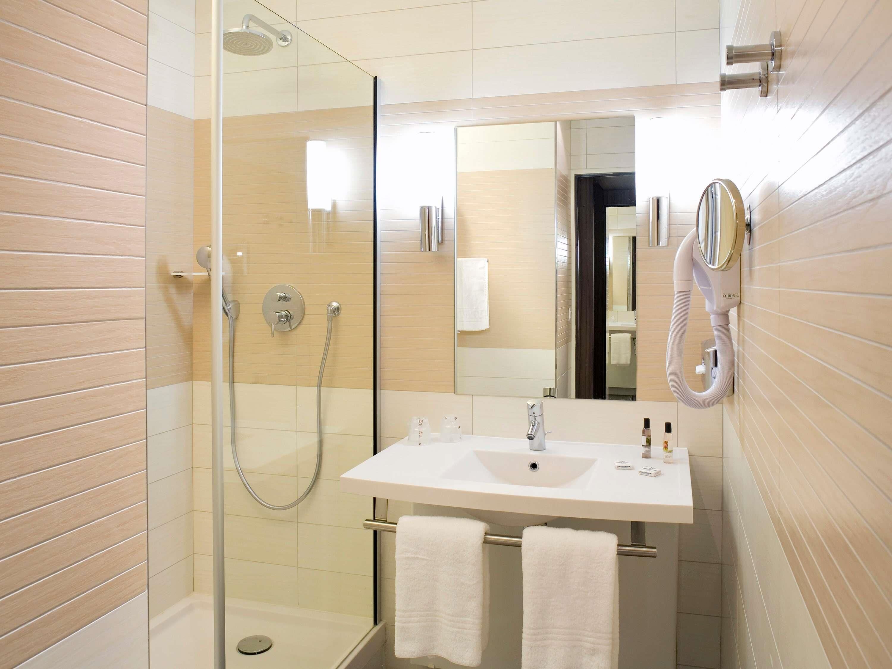 Ein modernes Badezimmer mit einer gläsernen Dusche, einem weißen Waschbecken mit Spiegel darüber und zwei Handtüchern an einem Ablagekorb.