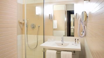 Ein modernes Badezimmer mit einer gläsernen Dusche, einem weißen Waschbecken mit Spiegel darüber und zwei Handtüchern an einem Ablagekorb.