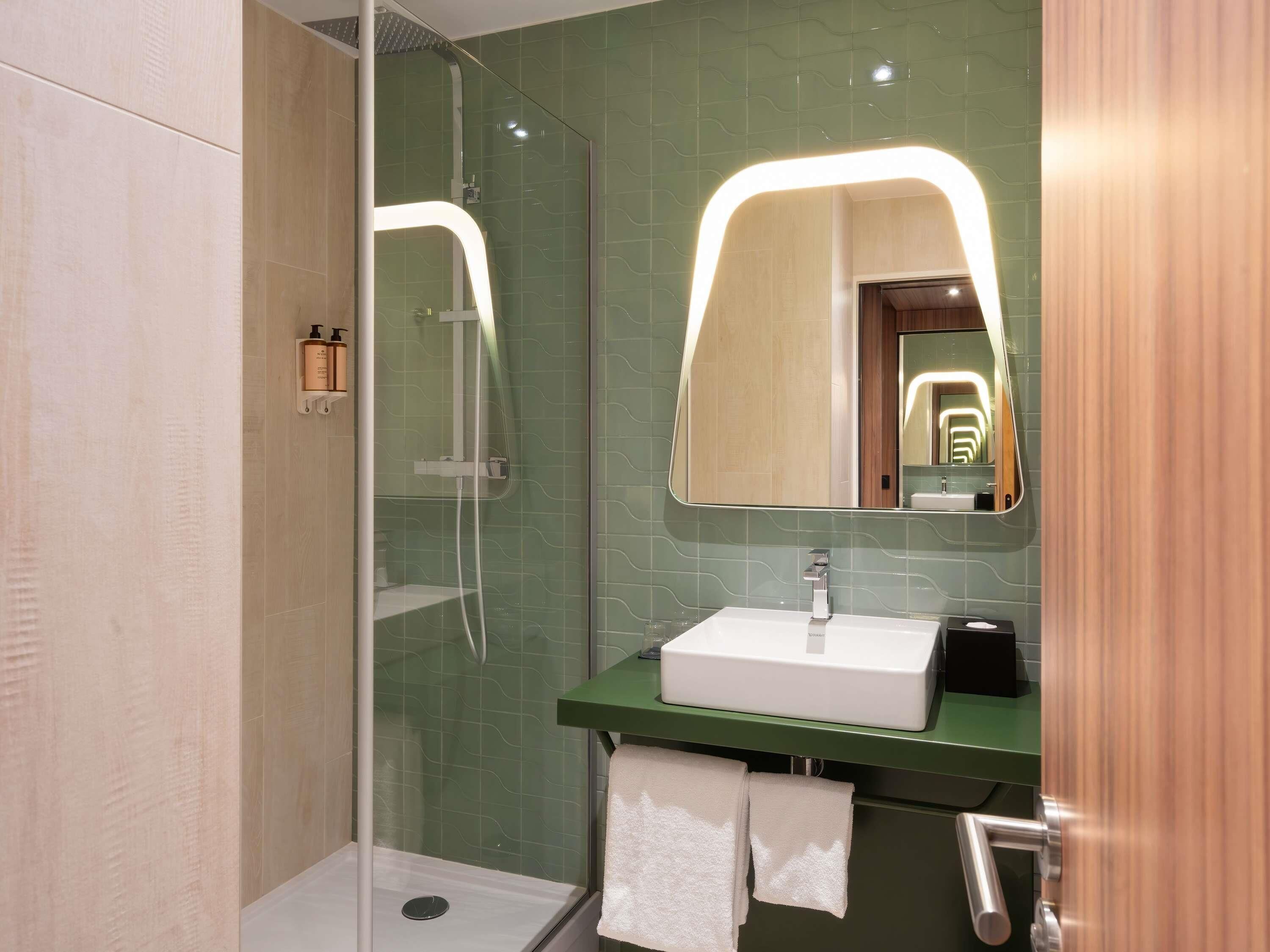 A modern bathroom with a glass-enclosed shower, a white sink, and a green countertop.
