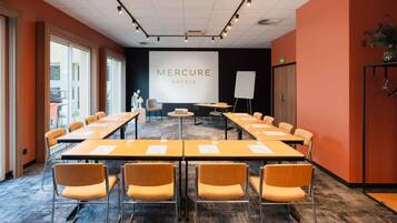 Een vergaderruimte met een lange tafel, stoelen, een whiteboard en een projectiescherm waarop 'MERCURE HOTELS' staat.