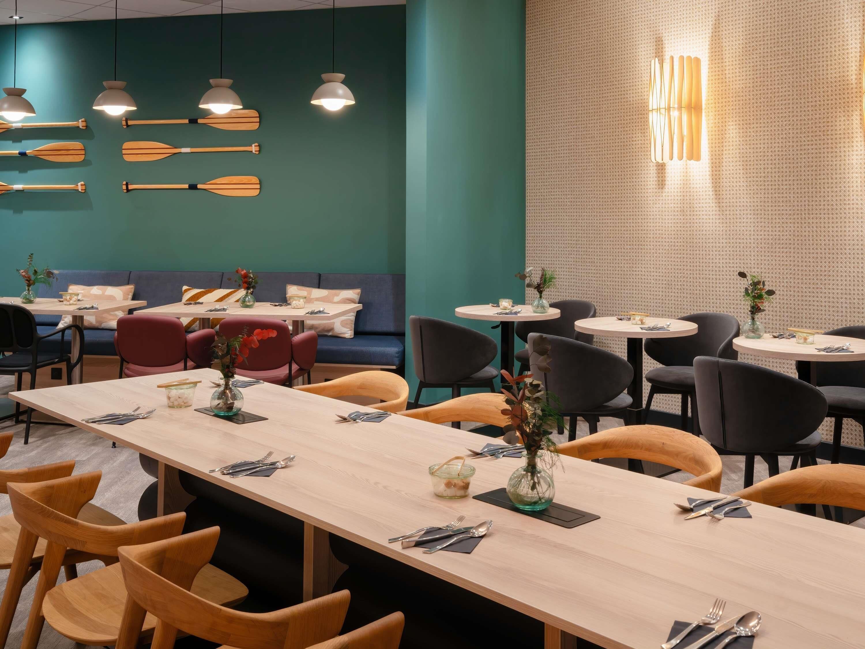 Un interno ristorante con tavoli e sedie in legno e una parete color acquamarina con palette di legno.