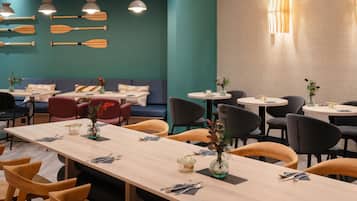 Un interno ristorante con tavoli e sedie in legno e una parete color acquamarina con palette di legno.