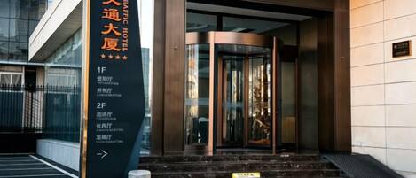 A modern building entrance with a glass door, a black sign with text, and a staircase leading up to the entrance.