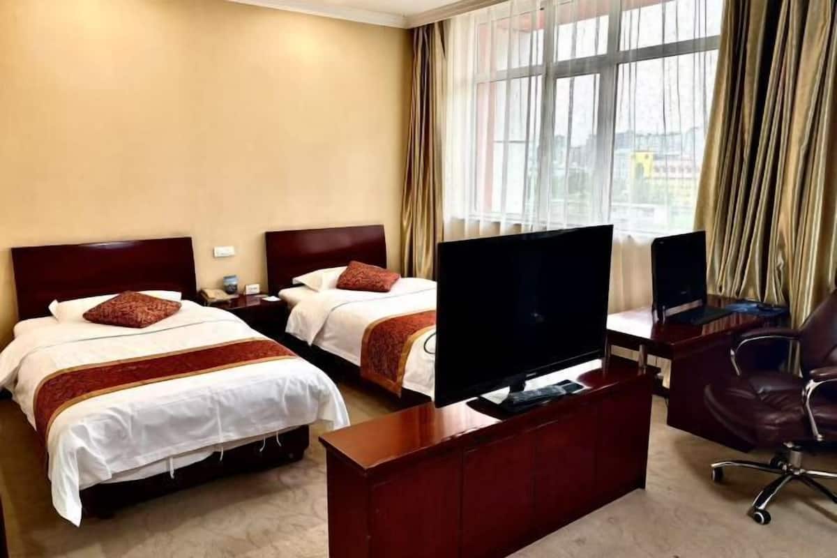 Ein Hotelzimmer mit zwei Betten, einem Fernseher, einem Schreibtisch und einem Stuhl.