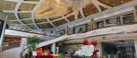 Interior de um grande shopping com várias lojas, um imponente candelabro, escadas rolantes e uma exposição floral central.