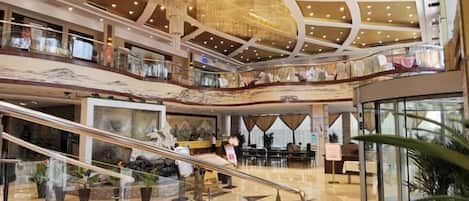 A multi-level shopping mall interior with escalators, glass railings, and decorative ceiling lights.
