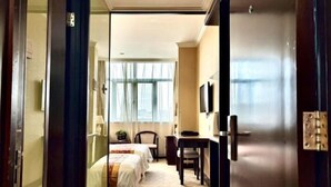 Een hotelkamer met twee bedden, een bureau, een stoel, een televisie en een groot raam.