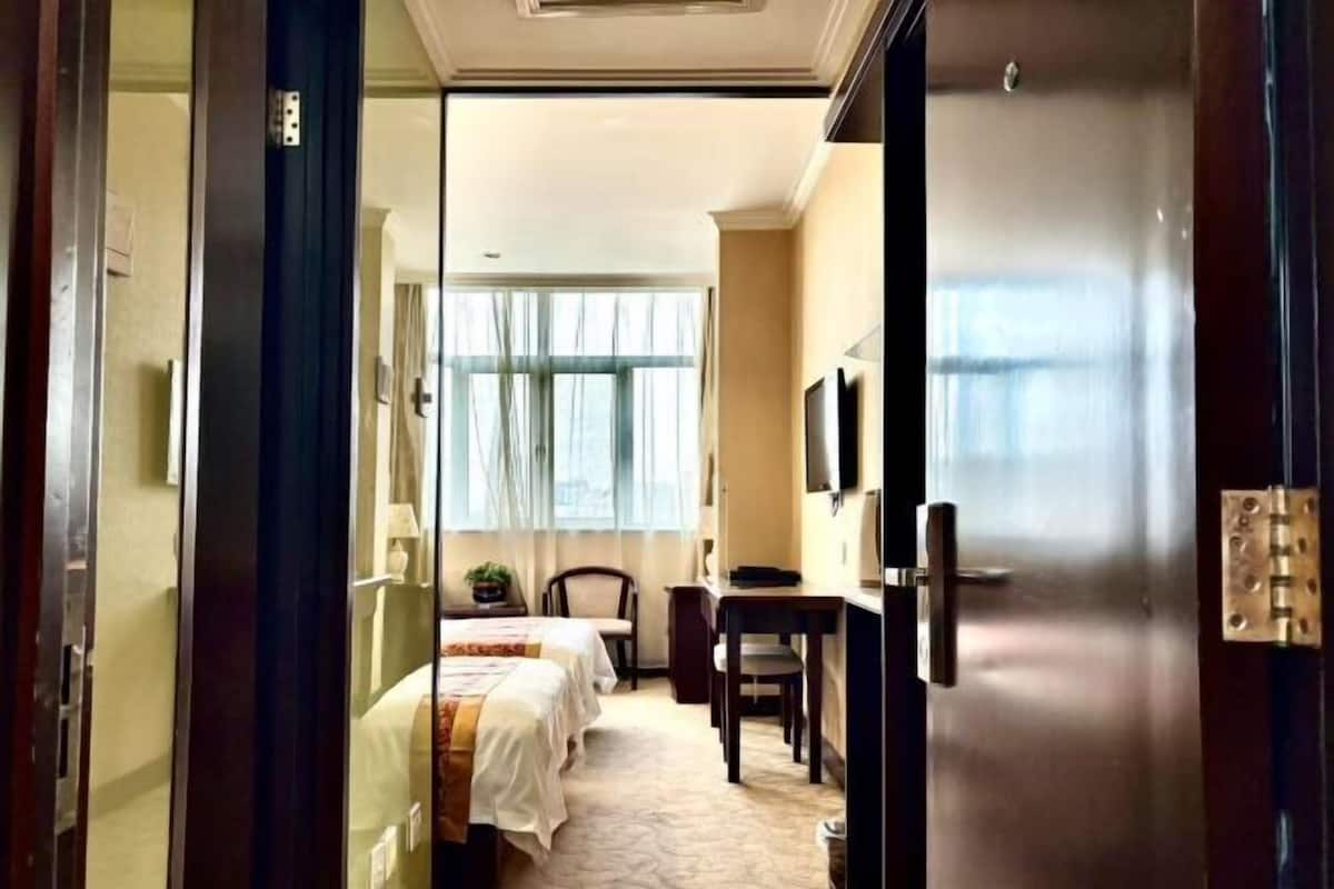 Ein Hotelzimmer mit zwei Betten, einem Schreibtisch, einem Stuhl, einem Fernseher und einem großen Fenster.