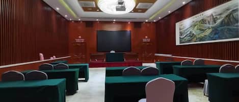 Un salón de conferencias con varias mesas, una pantalla grande y un cuadro en la pared.