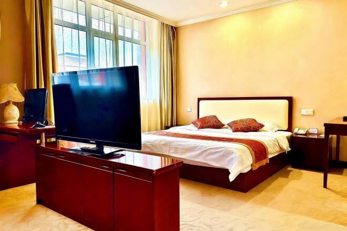 Ein Hotelzimmer mit einem Bett, einem Fernseher auf einer Holzkommode und einem Fenster mit Vorhängen.
