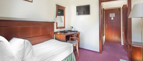 Una habitación de hotel con cama, escritorio, silla, televisor y una puerta que da a otra habitación.