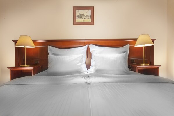 A neatly made bed with white linens and two bedside lamps on wooden nightstands.