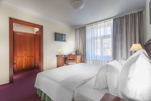 A hotel room with a bed, a desk, a chair, a television, and a window with curtains. - Hotel Lunik (Prague)