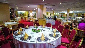 Un salón de banquetes con mesas redondas dispuestas para comer, piso de alfombra roja y sillas con marco dorado.