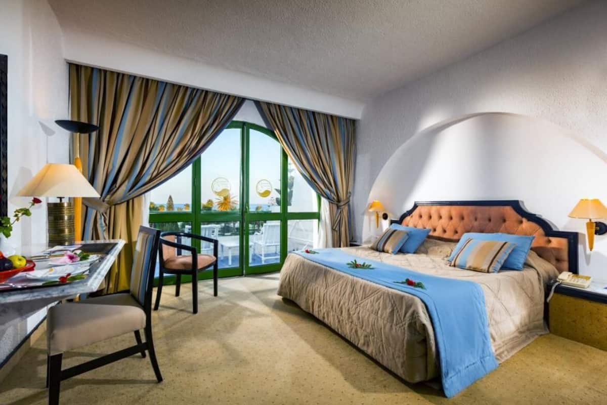 Ein Hotelzimmer mit Bett, Schreibtisch, Stuhl und Blick durch große Fenster.