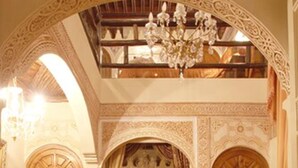 A traditional room with a high ceiling, ornate wooden doors, a bed with red bedding, and a chandelier. - Riad Catalina (Marrakech)