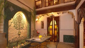A dining area with a table set for two, a tiled wall with a decorative arch, and a door with a glass panel. - Riad Catalina (Marrakech)