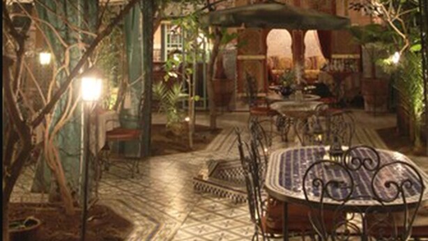 An outdoor patio with a table and chairs, surrounded by greenery and architectural details. - Riad Catalina (Marrakech)