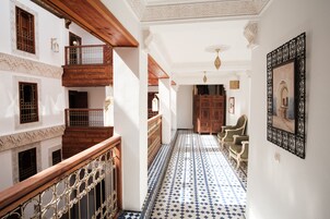 Um corredor com piso estampado, corrimãos de madeira e vista para um aposento com armário e cadeiras.