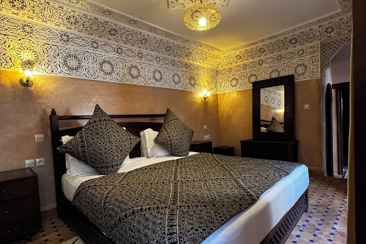 A bedroom with a patterned bedspread, a decorative ceiling, and a geometric patterned floor.