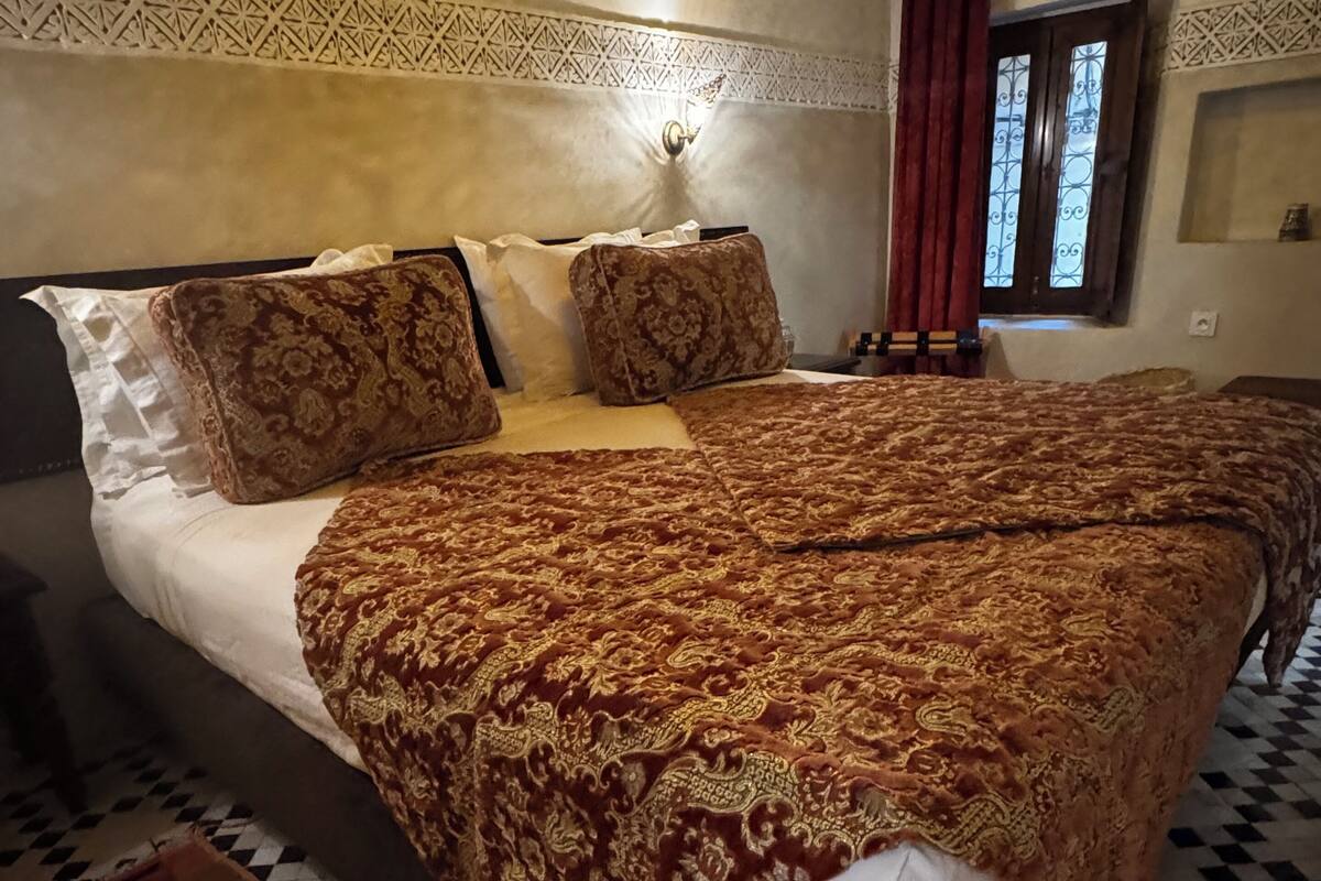 A bedroom with a large bed, patterned bedding, a checkered floor, and a window with curtains.