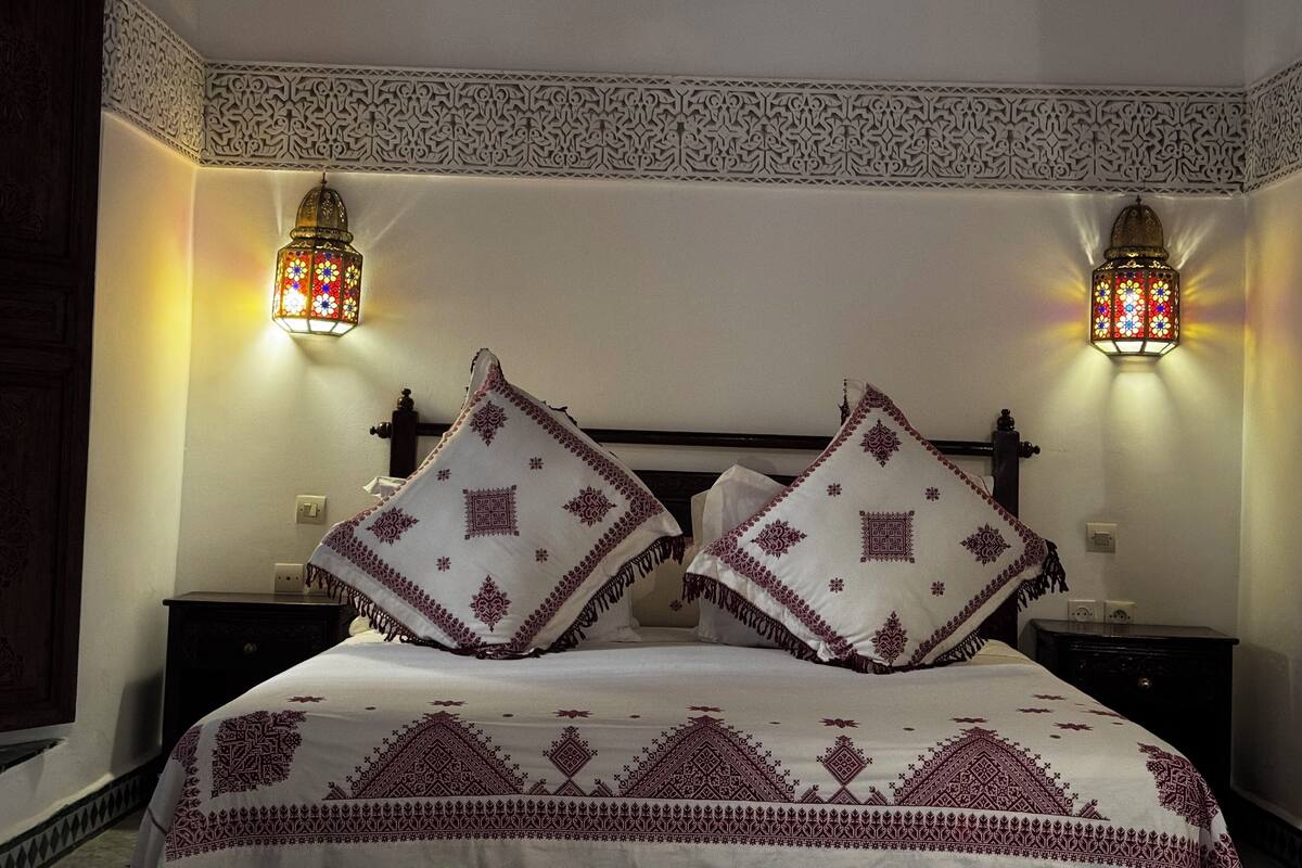 A bed with two pillows, a patterned bedspread, and two wall-mounted lamps.